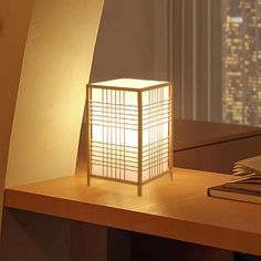 a lamp sitting on top of a wooden desk next to a book and window sill