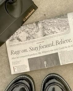 a pair of black shoes sitting on top of a floor next to a newspaper