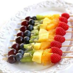 a white plate topped with cut up fruit and veggies on skewers