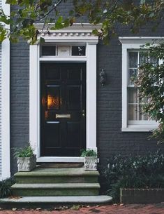 a black front door and steps in front of a gray house with white trim on the windows