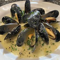 a white plate topped with mussels covered in sauce