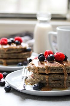 a stack of pancakes with berries and blueberries on top next to a glass of milk