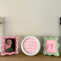 three decorative items sitting on top of a wooden shelf in front of a white wall