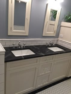 two sinks and mirrors in a bathroom with white tile flooring, blue walls and black counter tops