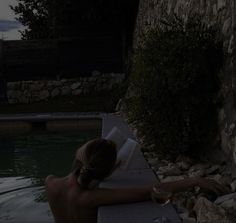 a woman is sitting in the water reading a book and drinking some wine at night