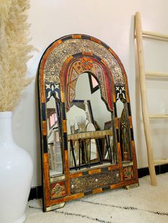 a mirror sitting next to a white vase on top of a carpeted floor in front of a wall