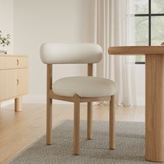 a white chair sitting next to a wooden table in front of a curtained window