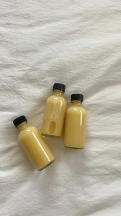 three jars with yellow liquid sitting on a white sheet