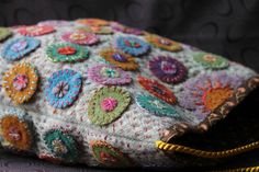 a purse with colorful flowers on it sitting on top of a black surface next to a gold zipper