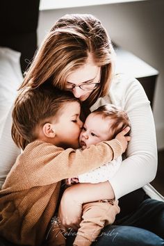 a woman holding two small children while sitting on a couch