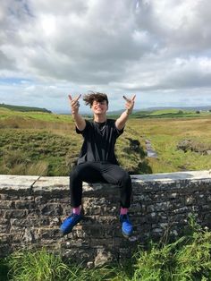 a man sitting on top of a stone wall with his hands up in the air