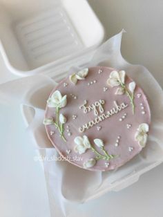 a pink birthday cake with white flowers on it sitting in a plastic container next to an empty tray