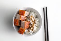 a white bowl filled with rice and tofu next to chopsticks