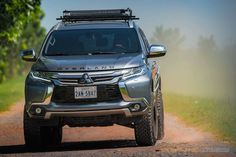 the front end of a silver four - doored suv driving down a dirt road