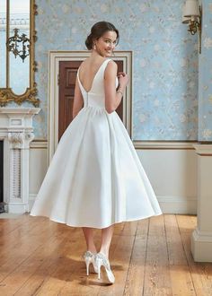 a woman in a white dress standing on a wooden floor next to a mirror and fireplace