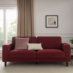 a red couch sitting in front of a window next to a table with a potted plant