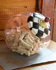 a glass bowl filled with dog treats on top of a wooden table next to a white and black checkered napkin