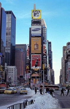 a city street filled with lots of traffic and tall buildings covered in snow on a sunny day