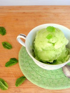 a cup filled with green ice cream on top of a wooden table next to mint leaves