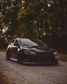 a black car parked on the side of a road next to some trees and bushes