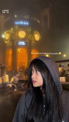 a woman with long black hair standing in front of a clock tower at night time