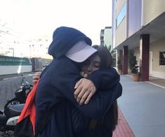 two people hugging each other on the sidewalk near a motor scooter and building