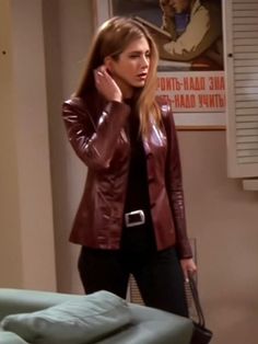 a woman in a leather jacket talking on her cell phone while standing next to a bed