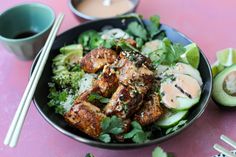 a bowl filled with chicken, cucumber and rice next to chopsticks