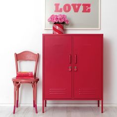 a red cabinet and pink chair in front of a white wall with a love sign above it