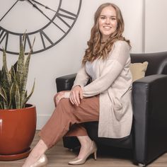 a woman sitting in a chair next to a plant and a clock on the wall