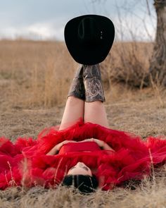 a woman laying on the ground wearing a red dress and black hat with her legs crossed