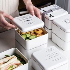 four white containers with food in them sitting on a table next to two people's hands