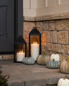 some white and black pumpkins are sitting on the front steps next to a lantern