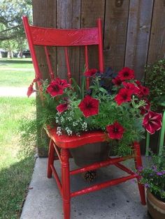 a red chair with potted flowers in it sitting on the side of a house