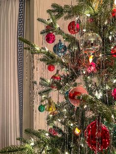 a christmas tree with ornaments hanging from it's branches in front of a window