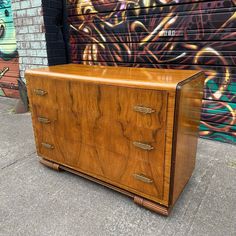 a wooden dresser sitting on top of a sidewalk next to a wall with graffiti painted on it