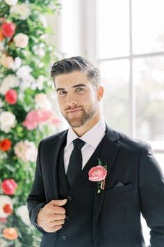 a man wearing a suit and tie standing in front of flowers