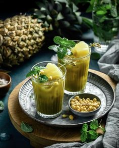 two glasses filled with green drinks on top of a plate