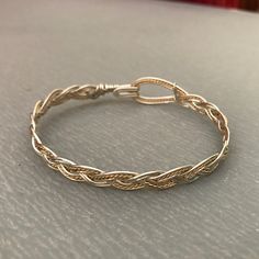 These bracelets are braided using a standard three-strand pattern, just like you would use when braiding hair or rope. The large hook and eye closure is part of the entire design, and allow the wearer to hook and unhook the bracelet with one hand; no helper should be needed! I have two variants: silver with a twisted gold wire as an accent and gold with a twisted silver wire. I make them in a range of sizes (in 1/4 inch increments) to fit any wrist. Yes! Sizes!! To determine the size you need, m Wire Jewelry Closures, Twisted Wire Bracelet, Braided Wire Bracelet, Adjustable Metal Jubilee Braided Bracelets, Adjustable Modern Twist Bracelet, Adjustable Braided Bangle Jewelry, Adjustable Bracelet With A Modern Twist, Adjustable Braided Bracelet Jewelry, Adjustable Braided Jewelry Bracelet