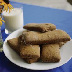 some cookies on a white plate next to a glass of milk and a vase with flowers