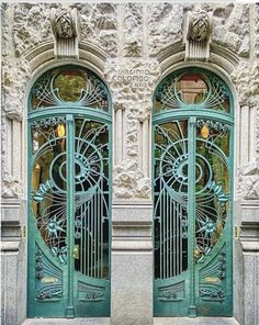 two green doors are open in front of a stone building with ornate carvings on it