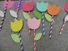 paper flowers and straws are arranged on a gray surface with colorful striped drinking straws