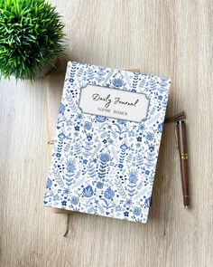 a blue and white notebook sitting on top of a wooden table next to a pen