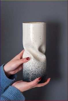 a woman holding a white and black vase in her hand with red nail polish on it