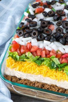 a layered salad with black olives, tomatoes, lettuce and other toppings