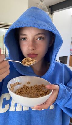 a girl in a blue hoodie eating cereal out of a bowl with a spoon