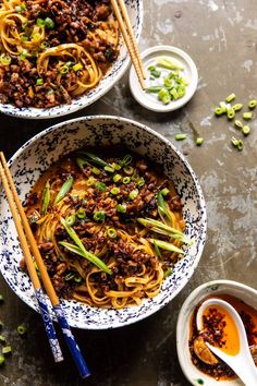 two bowls filled with noodles and vegetables next to chopsticks on a table top