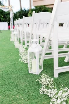 rows of white chairs lined up on the grass at a wedding ceremony with lanterns and baby's breath flowers