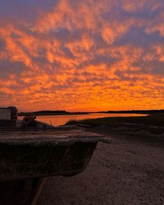 a boat sitting on top of a sandy beach under a colorful sky with clouds in the background