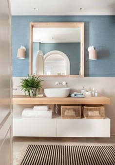 a white sink sitting under a large mirror next to a wooden shelf with baskets on it